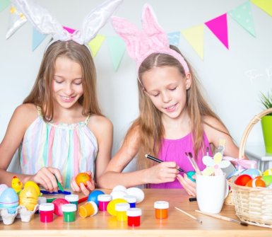 tween girls at a table in brighly colored clothing painting easter eggs and making easter crafts while wearing cute bunny ears
