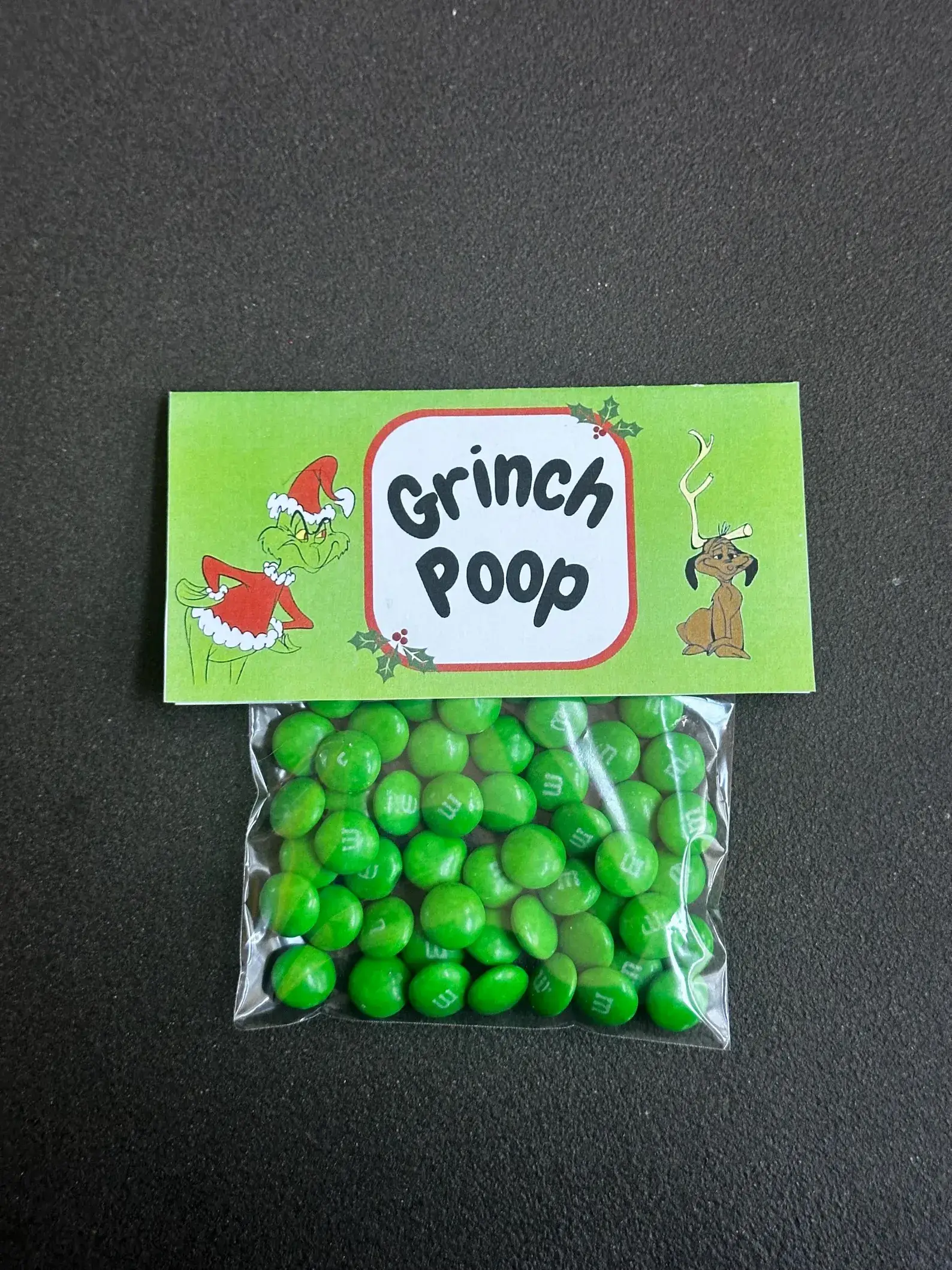 Clear bag filled with green candy-coated chocolates topped with a festive cartoon villain novelty label, a humorous and playful Christmas Eve Box idea for tweens.