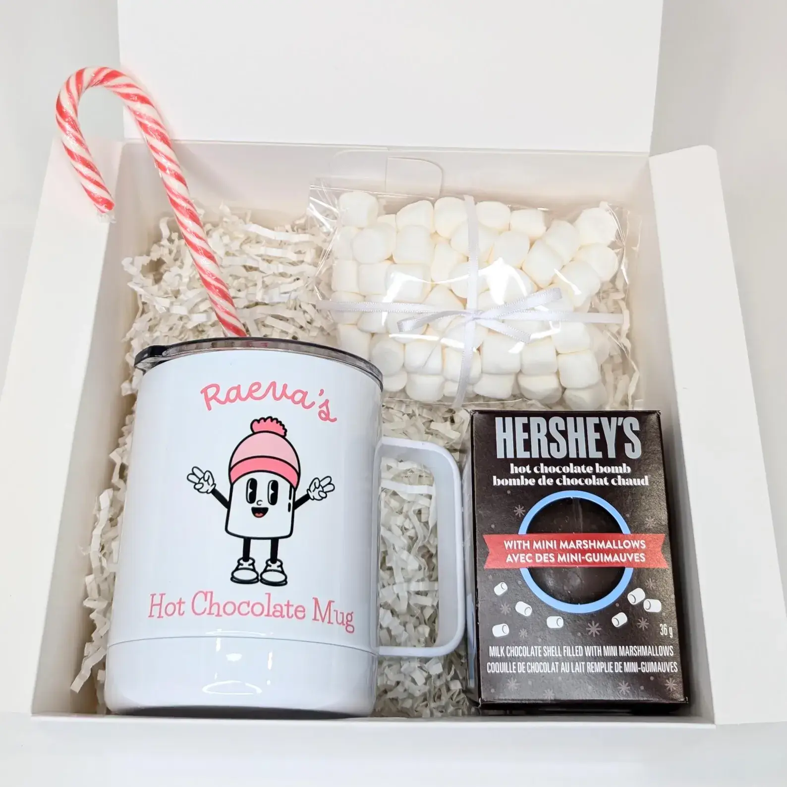 White gift box containing a personalized insulated mug with a cute marshmallow character, mini marshmallows, a chocolate bomb, and a candy cane, perfect for Christmas Eve Box ideas for tweens.