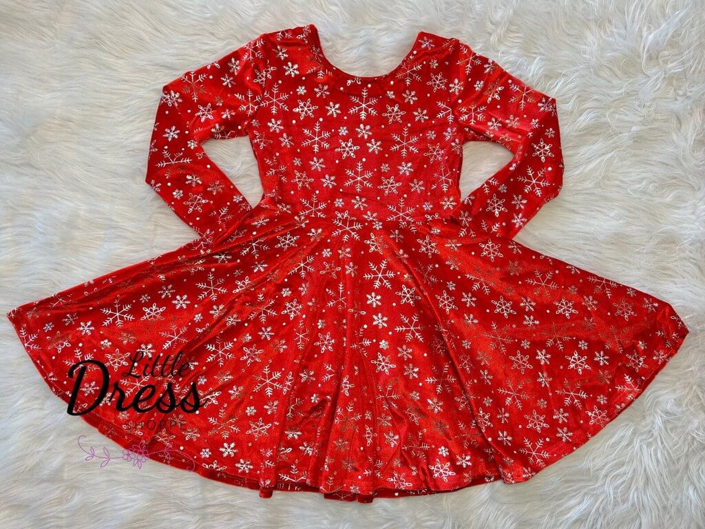 Long-sleeve red Christmas dress for tweens with a sparkly silver snowflake print and a twirl-worthy flared skirt, laid flat on faux fur.